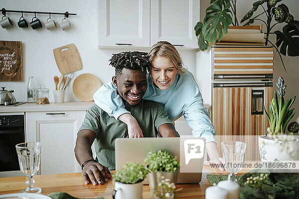 Woman with arm around man using laptop at home