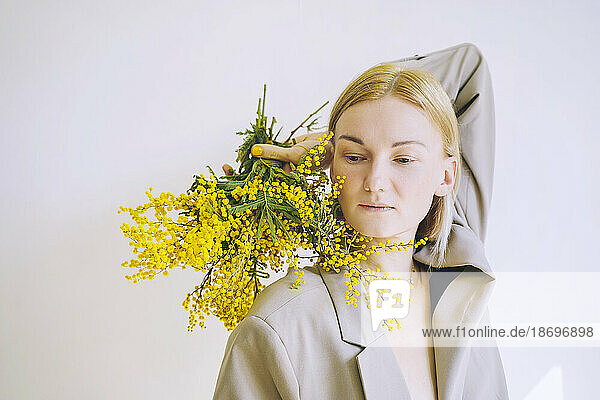 Contemplative woman holding bunch of mimosa flowers against white background