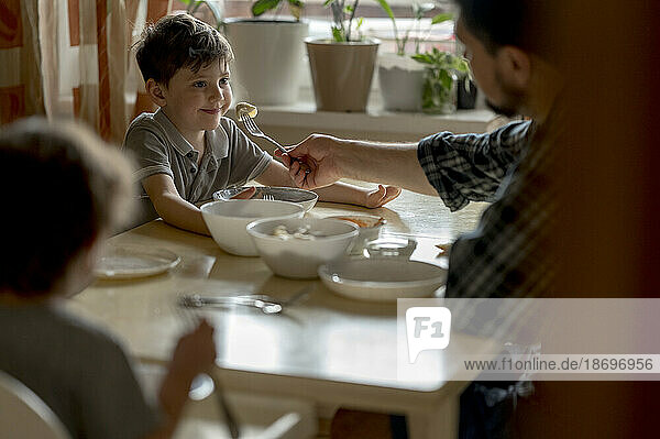 Father feeding dumpling to son at dining table in home