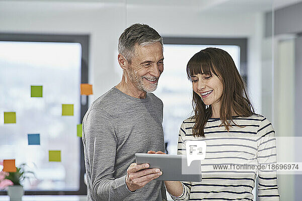 Businessman showing over tablet PC to smiling colleague in office