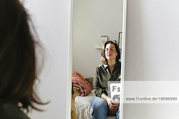 Reflection of woman in mirror by wall at home