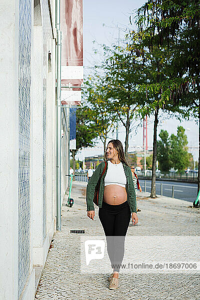 Lächelnde schwangere Frau  die auf dem Bürgersteig läuft