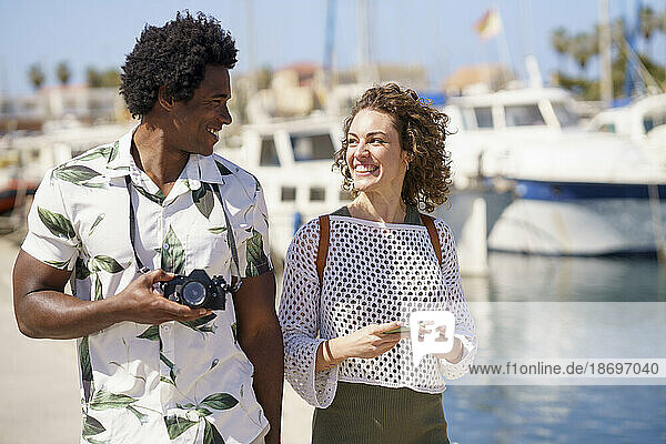 Cheerful couple with camera walking at harbour