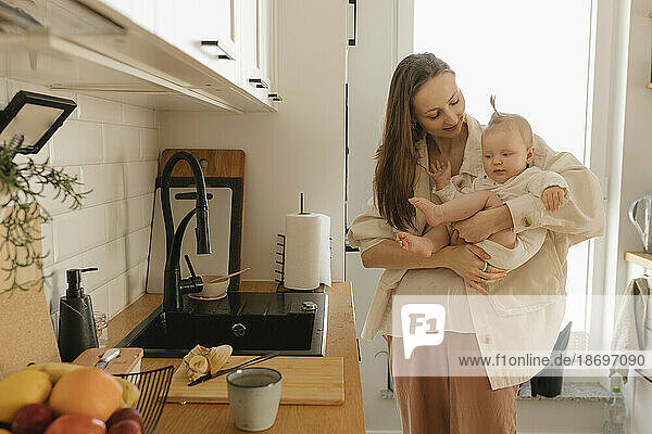 Smiling mother carrying daughter by kitchen counter at home