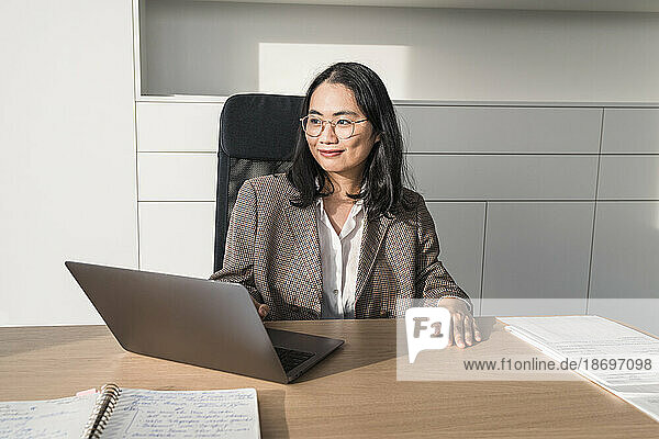 Nachdenkliche Geschäftsfrau sitzt mit Laptop am Schreibtisch im Büro