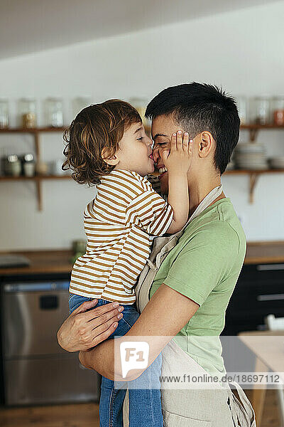 Son kissing mother on nose in kitchen at home
