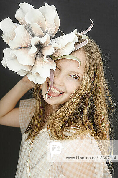 Blondes Mädchen streckt die Zunge heraus und hält eine Blume in der Hand