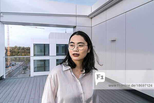 Thoughtful young businesswoman in white shirt on terrace of office building