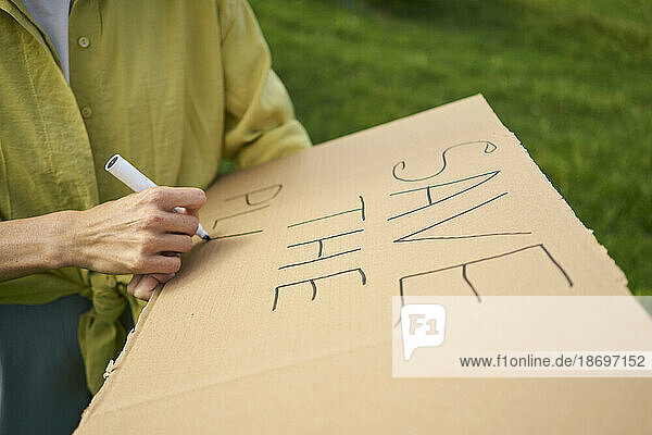 Frau schreibt mit Filzstift den Text „Save The Planet“ auf Karton  der im Garten ausgeschnitten ist
