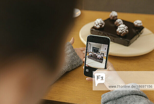 Woman photographing homemade cake with smart phone at home
