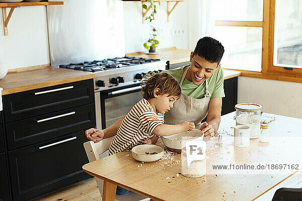 Mother and son preparing food at dining table in kitchen
