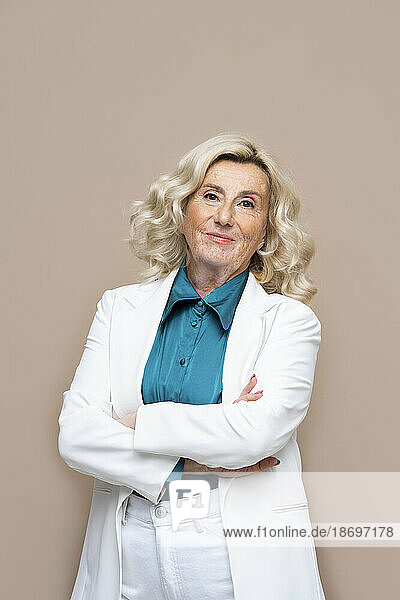 Senior businesswoman standing with arms crossed against beige background