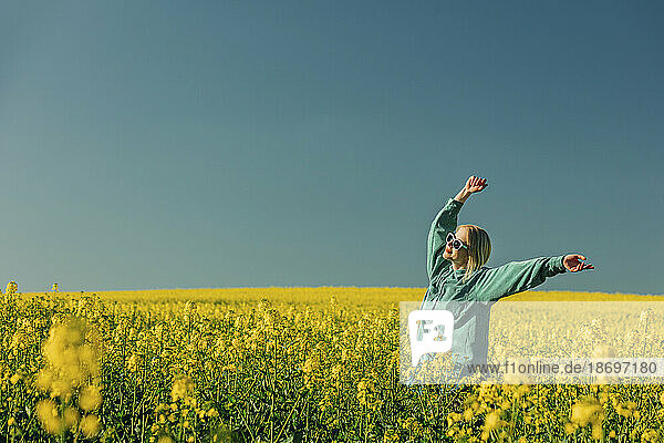 Carefree woman with arms raised standing in rapeseed field