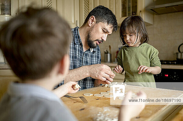 Father teaching children to make dumplings at kitchen