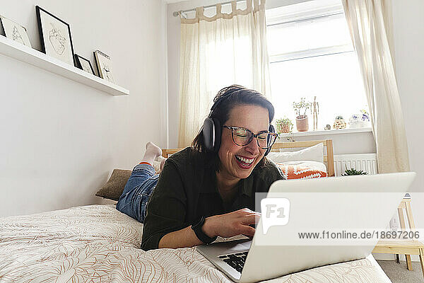 Happy freelancer with laptop lying on bed at home