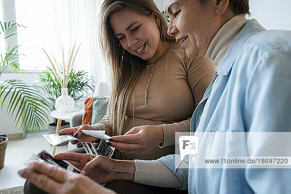 Senior woman looking at ultrasound photos with pregnant daughter at home