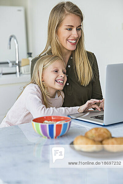 Smiling daughter learning to use laptop with mother at home