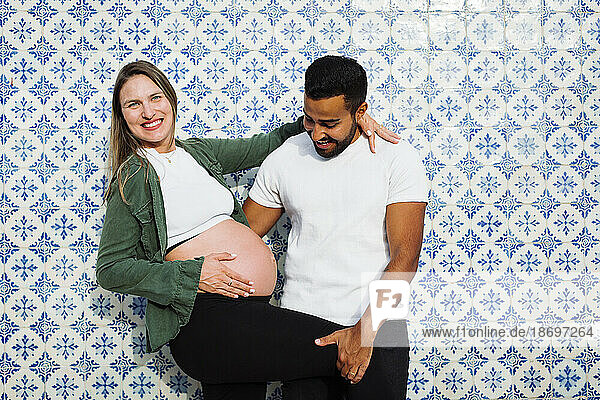 Happy man with pregnant woman in front of patterned tiled wall