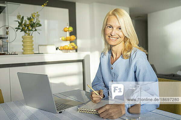 Smiling freelancer woman with laptop at desk in home office