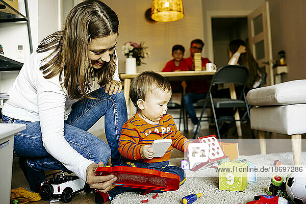 Mother crouching by son playing with toys at home