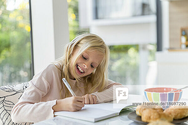 Smiling blond girl doing homework at home
