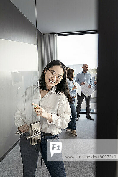 Porträt einer lächelnden jungen Geschäftsfrau  die einen Laptop mit Kollegen im Hintergrund im Büro benutzt