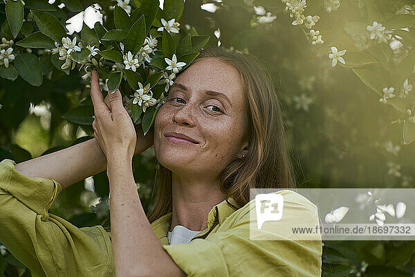 Lächelnde Frau neben blühendem Baum im Garten
