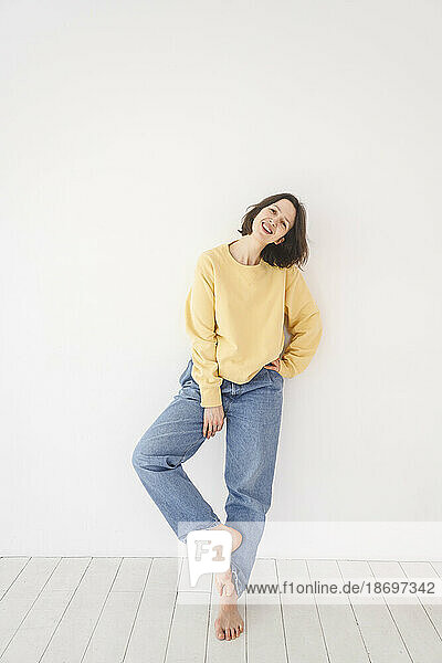 Smiling woman in casual clothes leaning on white wall
