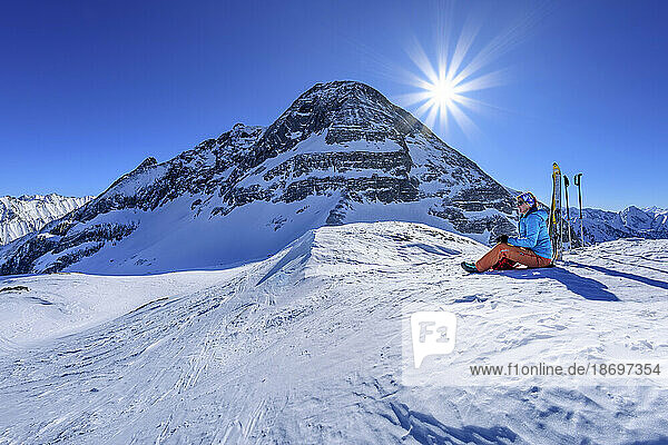 Österreich  Tirol  Sonne scheint über einer Skifahrerin  die am Torhelm eine Pause macht