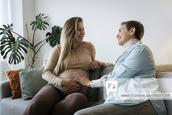 Senior woman with pregnant daughter sitting on sofa at home