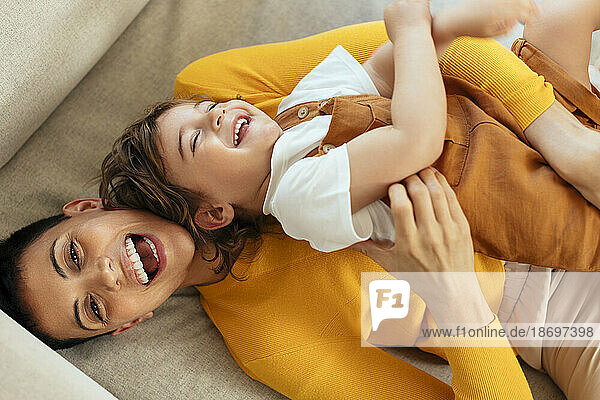Fröhliche Frau kitzelt ihren Sohn zu Hause auf dem Sofa