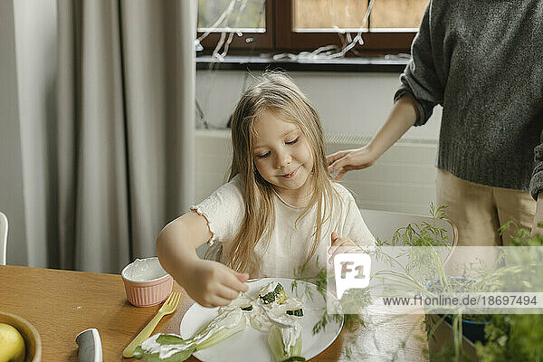 Mädchen macht Kreativität mit Gemüse auf dem Teller der Mutter zu Hause