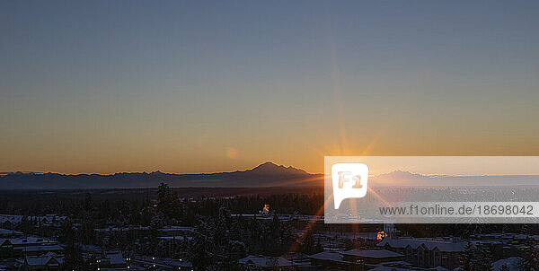 Sunburst over mountains and cityscape at sunset; Surrey  British Columbia  Canada