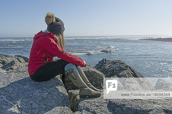 View of woman sitting on the rocks on the beach watching the ice bergs float by along the South Coast of Iceland; Jokulsarlon  South Iceland  Iceland