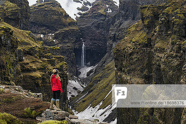 Woman standing and overlooking Mulagljufur Canyon  a hikers paradise  watching an amazing view of a waterfall and the moss-covered cliffs; Vik  South Iceland  Iceland