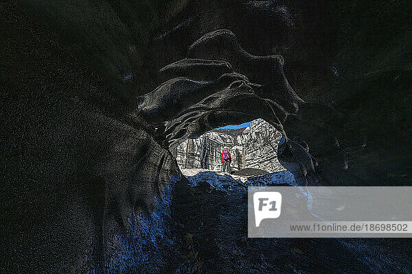 View through an ice cave of a woman exploring a glacier while traveling in Iceland; Vik  South Iceland  Iceland