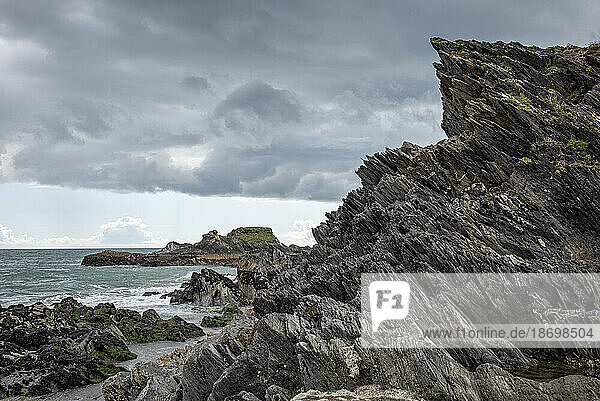 Close-up of jagged rock formations and rocky shoreline of the Atlantic Ocean along the beach at Long Strand under a cloudy sky; Castlefreke  West Cork  Ireland