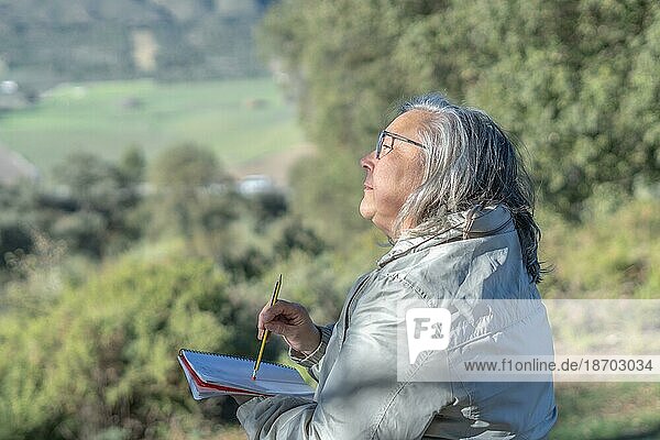 Frau mit einem Notizbuch und einem Bleistift in der Hand auf einem Feld  die den Horizont betrachtet und denkt
