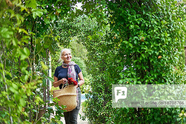 Happy senior woman walking under trellis in summer garden