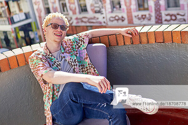 Portrait happy young albino man sitting on sunny urban rooftop
