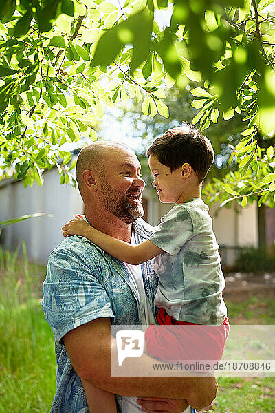 Happy father holding cute son with Down Syndrome in backyard
