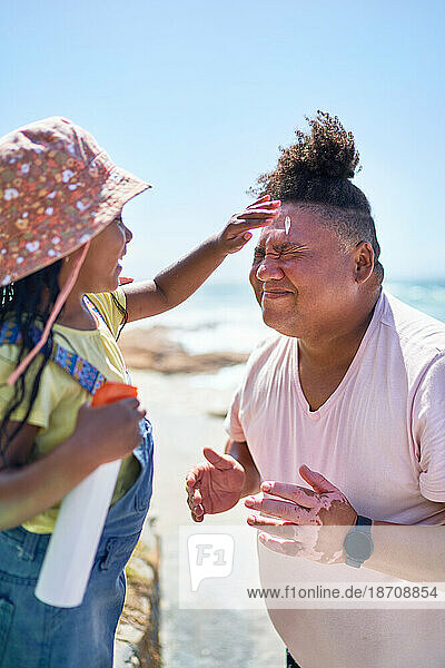 Cute daughter applying sunscreen to face of father on sunny beach