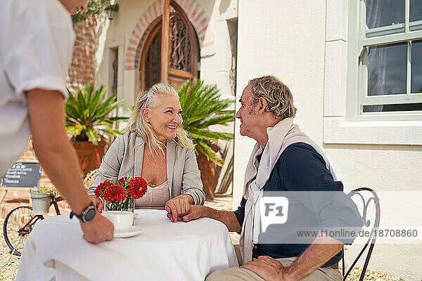 Waiter serving coffee to happy senior couple at sidewalk cafe table