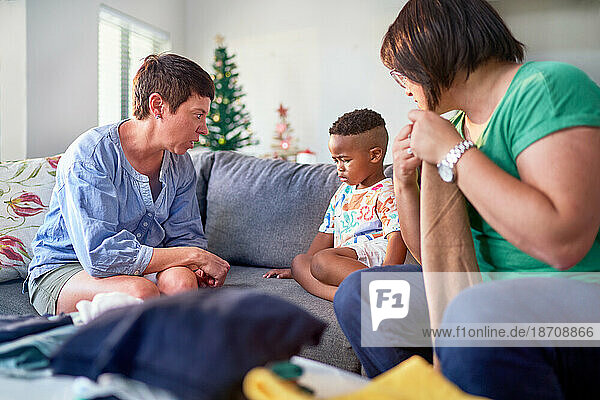 Lesbian couple scolding unhappy son on living room sofa