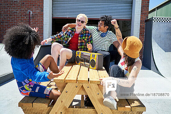 Happy young friends listening to music with boom box at picnic table