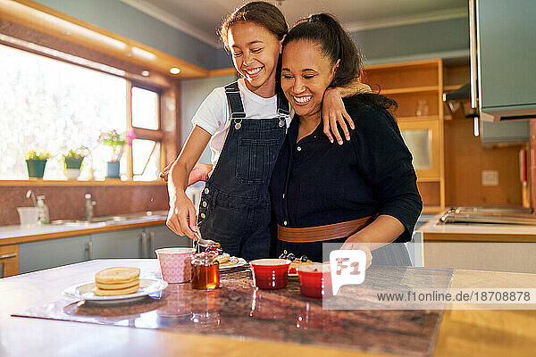 Happy mother and daughter eating pancakes in morning kitchen