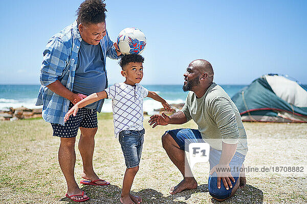Gay male couple and son playing with soccer ball on sunny beach
