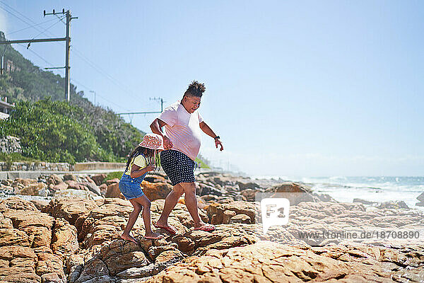 Barefoot father and daughter walking on rocks on sunny beach