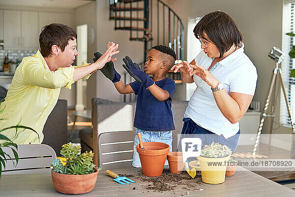 Playful lesbian couple and son gesturing  planting plants on patio