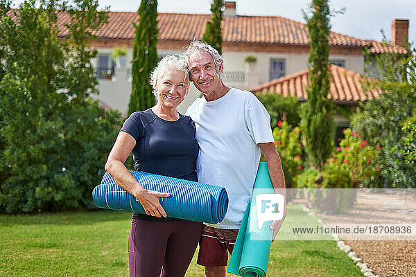 Portrait happy  active senior couple with yoga mats in villa garden